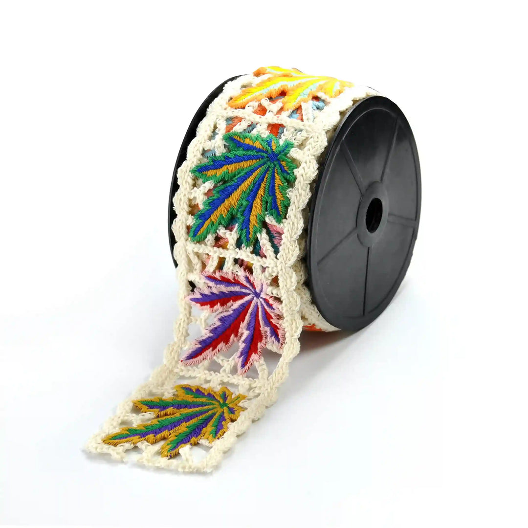 Colorful crochet lace with leaf pattern on a spool against a white background