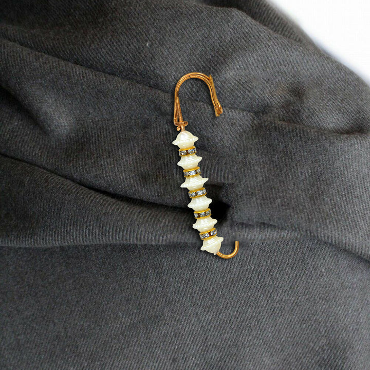 Decorative brooch with white stones and gold accents on a dark fabric background