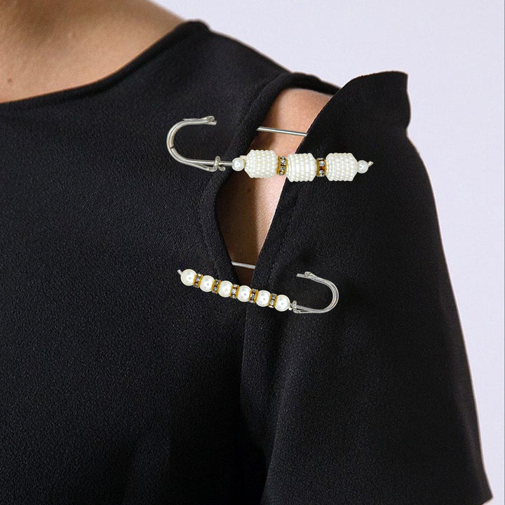 Ani Accessories Pearl and metal brooches on a black garment against a white background