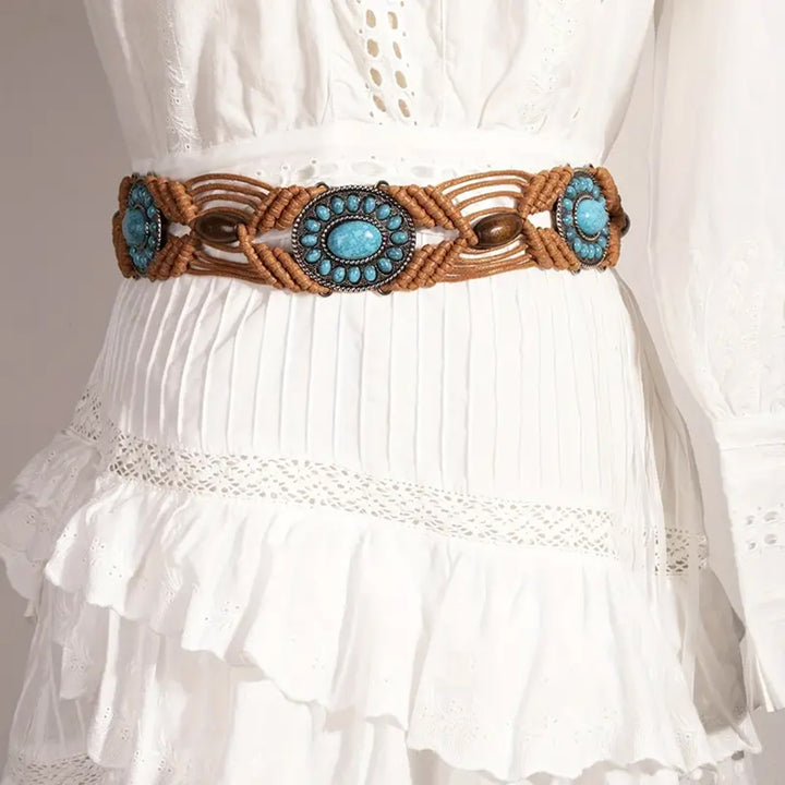 Ani Accessories Womens Belt A tan/light brown macrame belt with oval turquoise-colored stone medallions and wooden beads, tied in a knot. The belt is displayed on a light, textured surface.