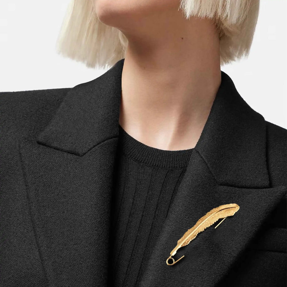 ani accessoires, model wearing black coat with a gold feather brooch on a plain background as a coat brooch & blazer brooch.
