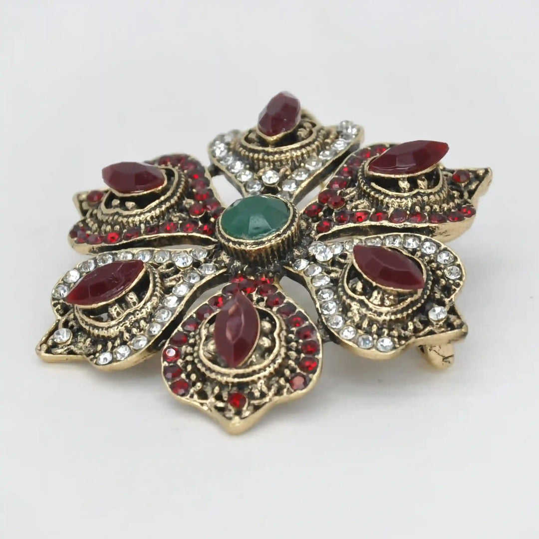 ANI Accessories antique gold flower brooch from an angle showing the raised red and green stones with white color background 
