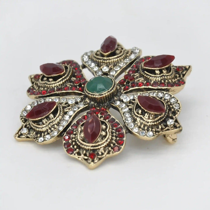 ANI Accessories antique gold flower brooch from an angle showing the raised red and green stones with white color background 
