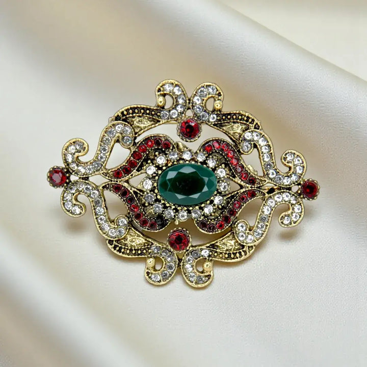 ANI Accessories baroque revival green stone brooch in antique gold with red and clear rhinestones on cream satin