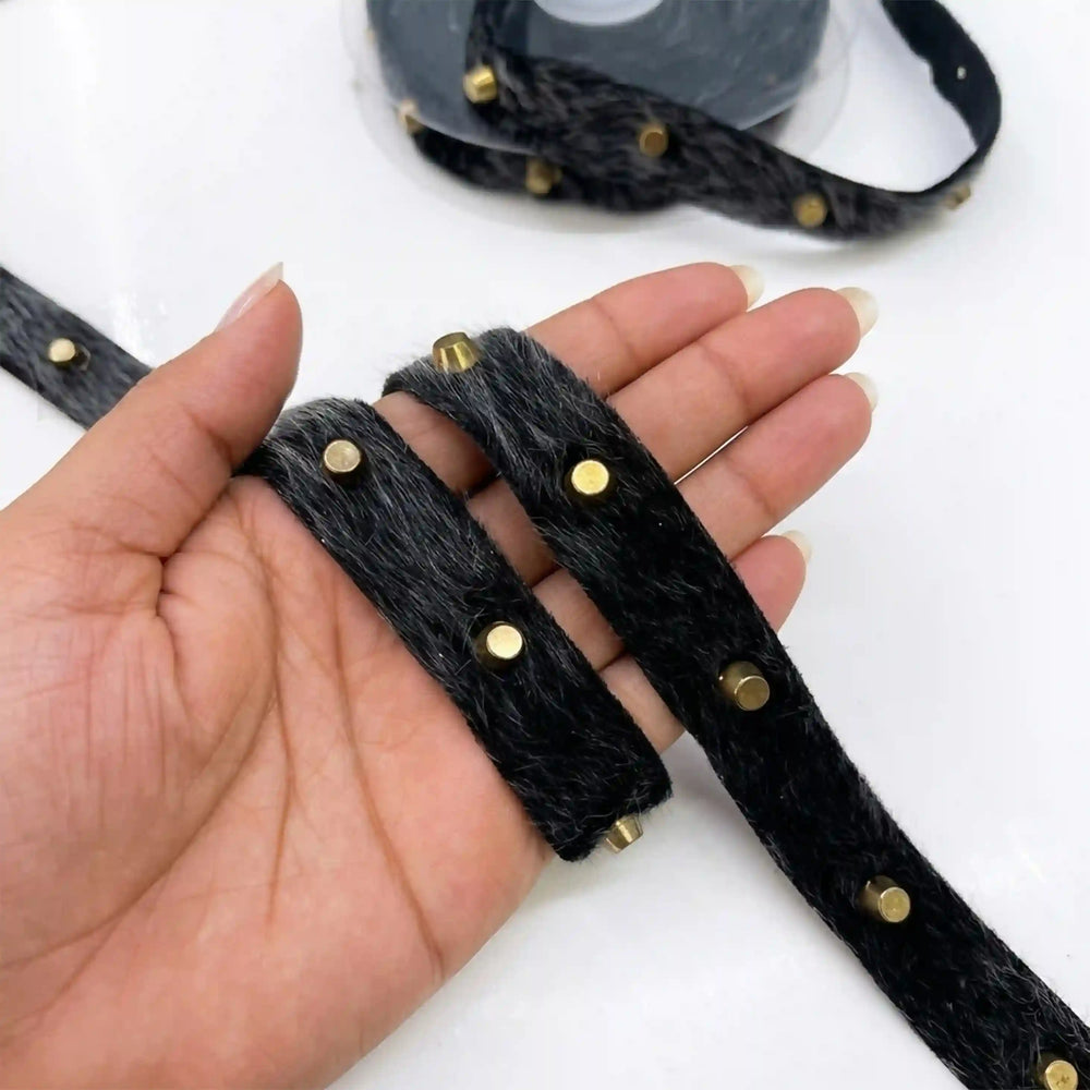 ANI Accessories black fur trim for jacket with gold studs held in hand with white color background 