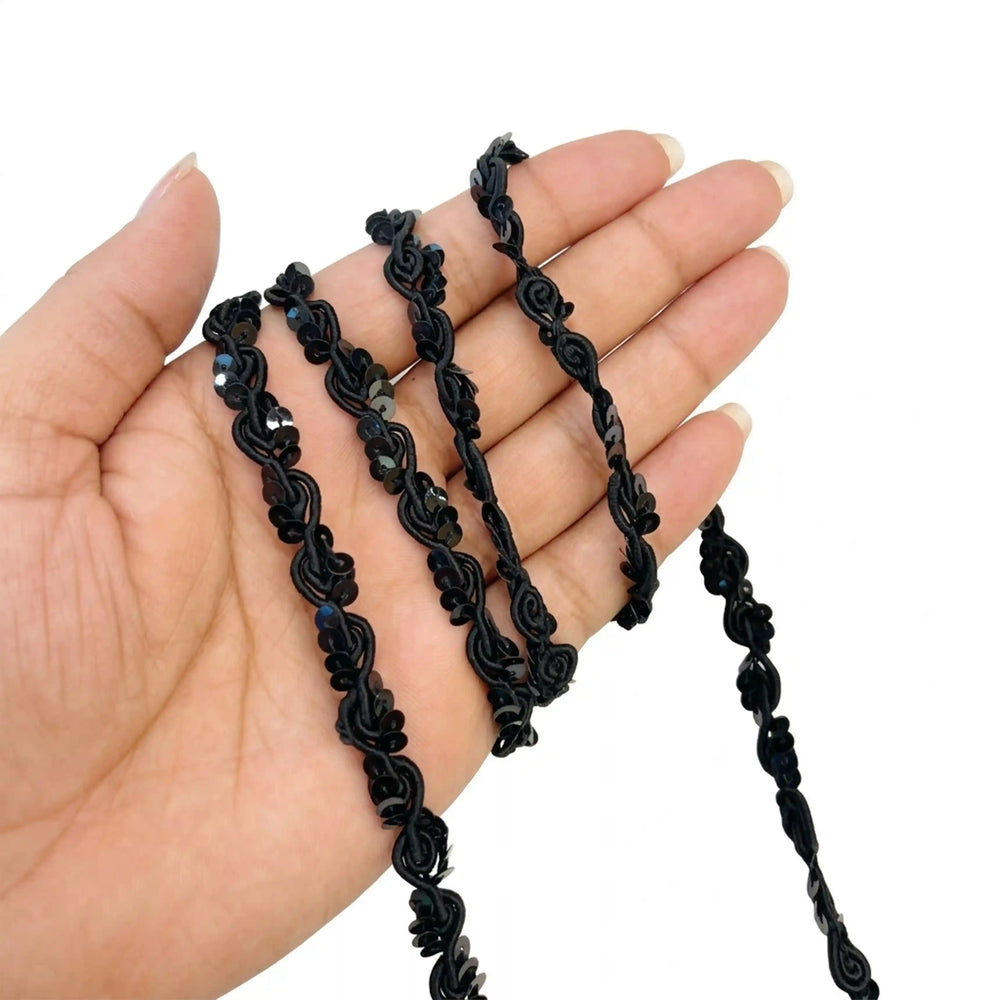 ANI Accessories black sequin braid trim held in hand in loose loops with white color background 
