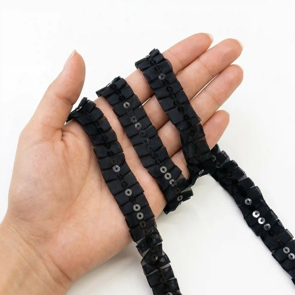 ANI Accessories black sitara lace held in hand to show the pleats and sequins with white color background 