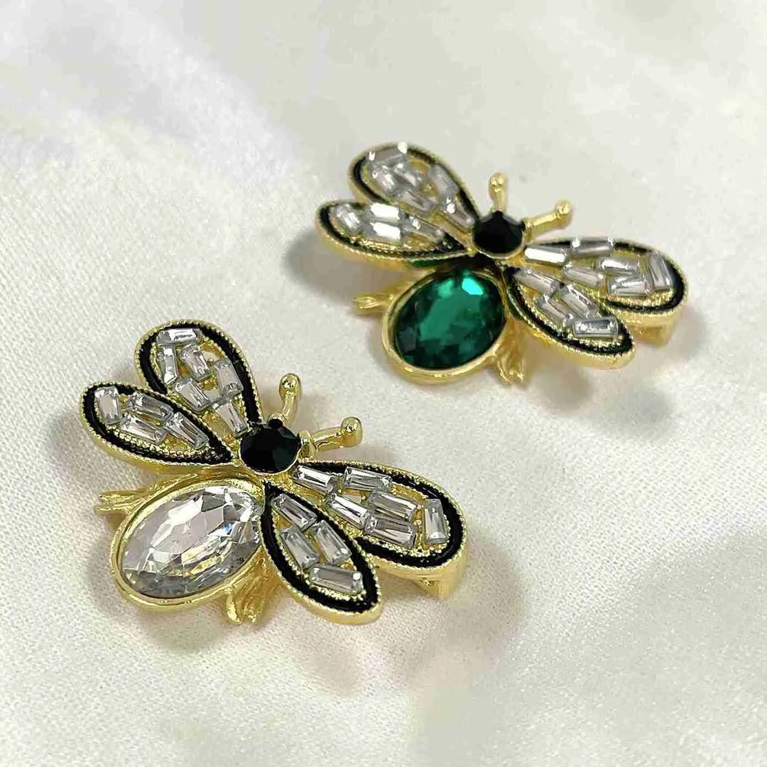 Emerald and white crystal bee brooches on white faux fur with white color background 