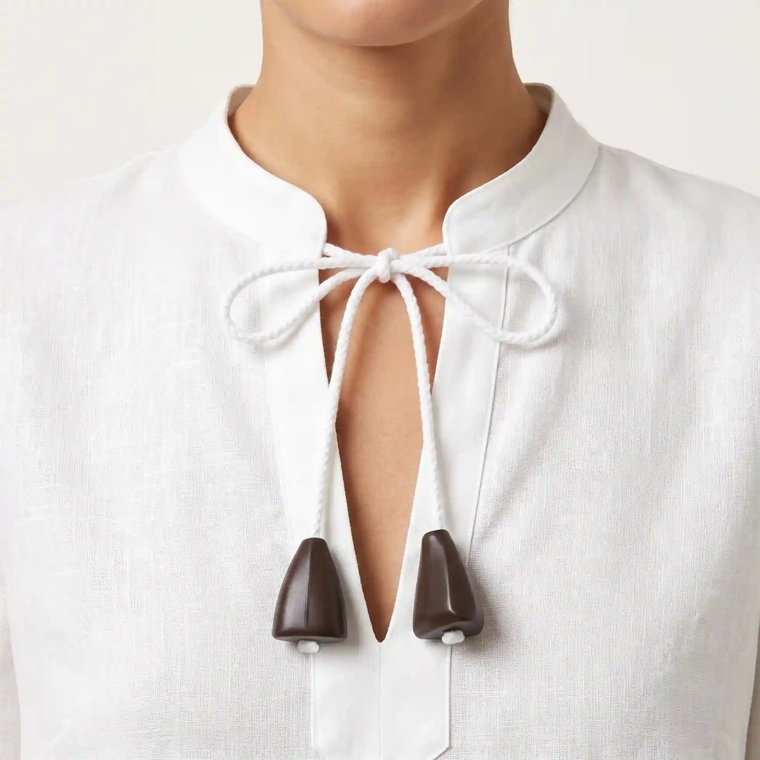ANI Accessories dark brown bell-shaped cord end caps on the white braided tie cord of a white linen band-collar kurta 
with color background 