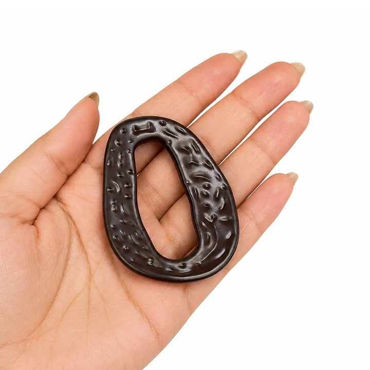 ANI Accessories dark brown hammered oval ring buckle resting in an open palm to show real size, on white color background 