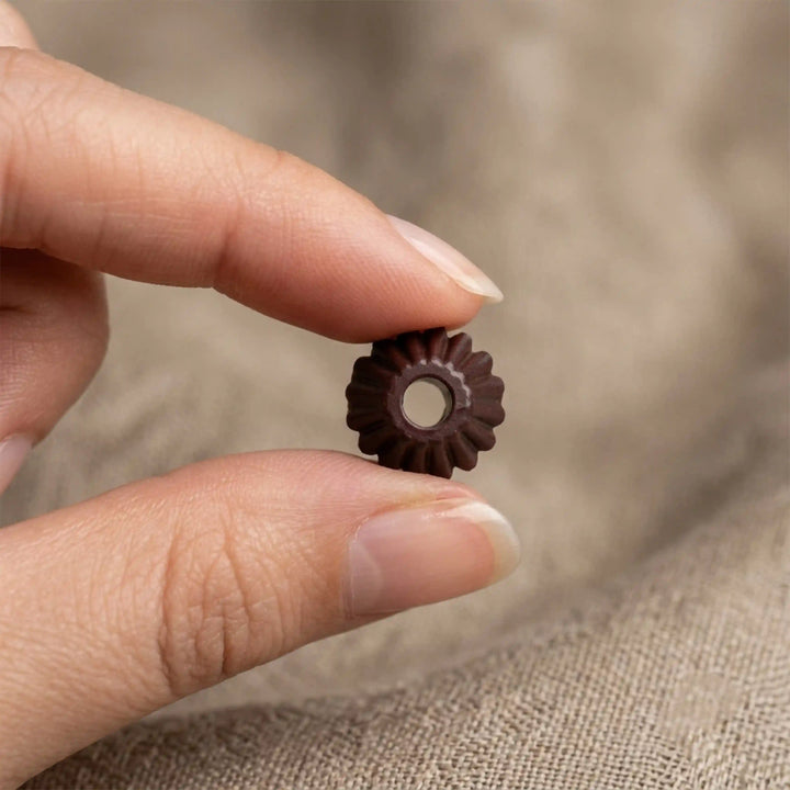ANI Accessories dark brown melon cord end bead held between fingertips, top view of fluted edge and centre hole on beige linen Background 