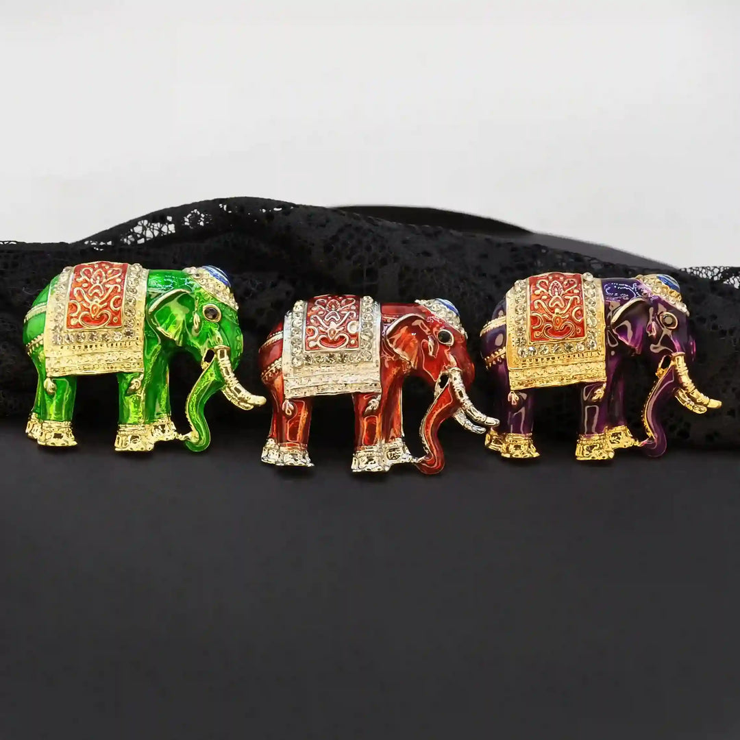 Green, red and purple elephant brooches lined up on black satin color background 