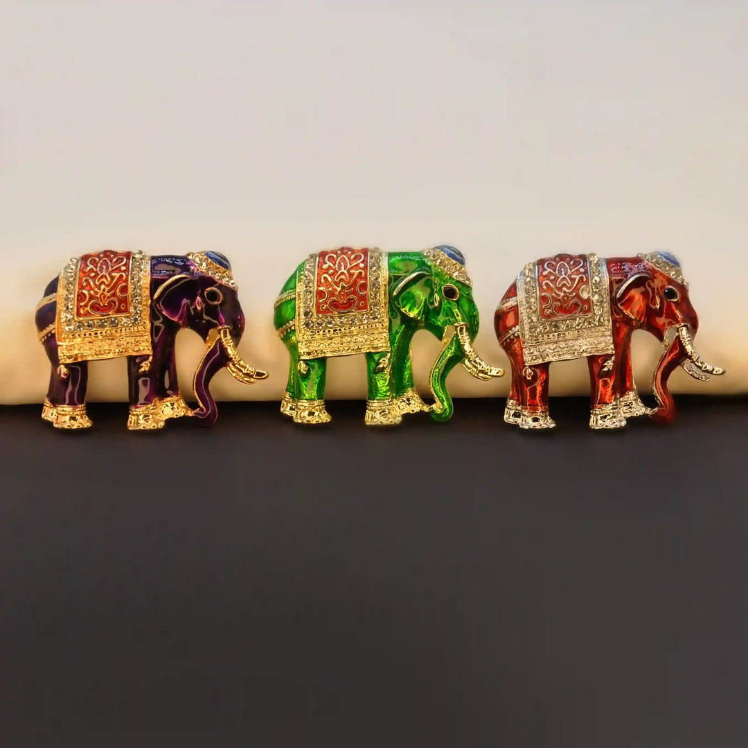 Three enamel elephant brooches in a row on a dark background 