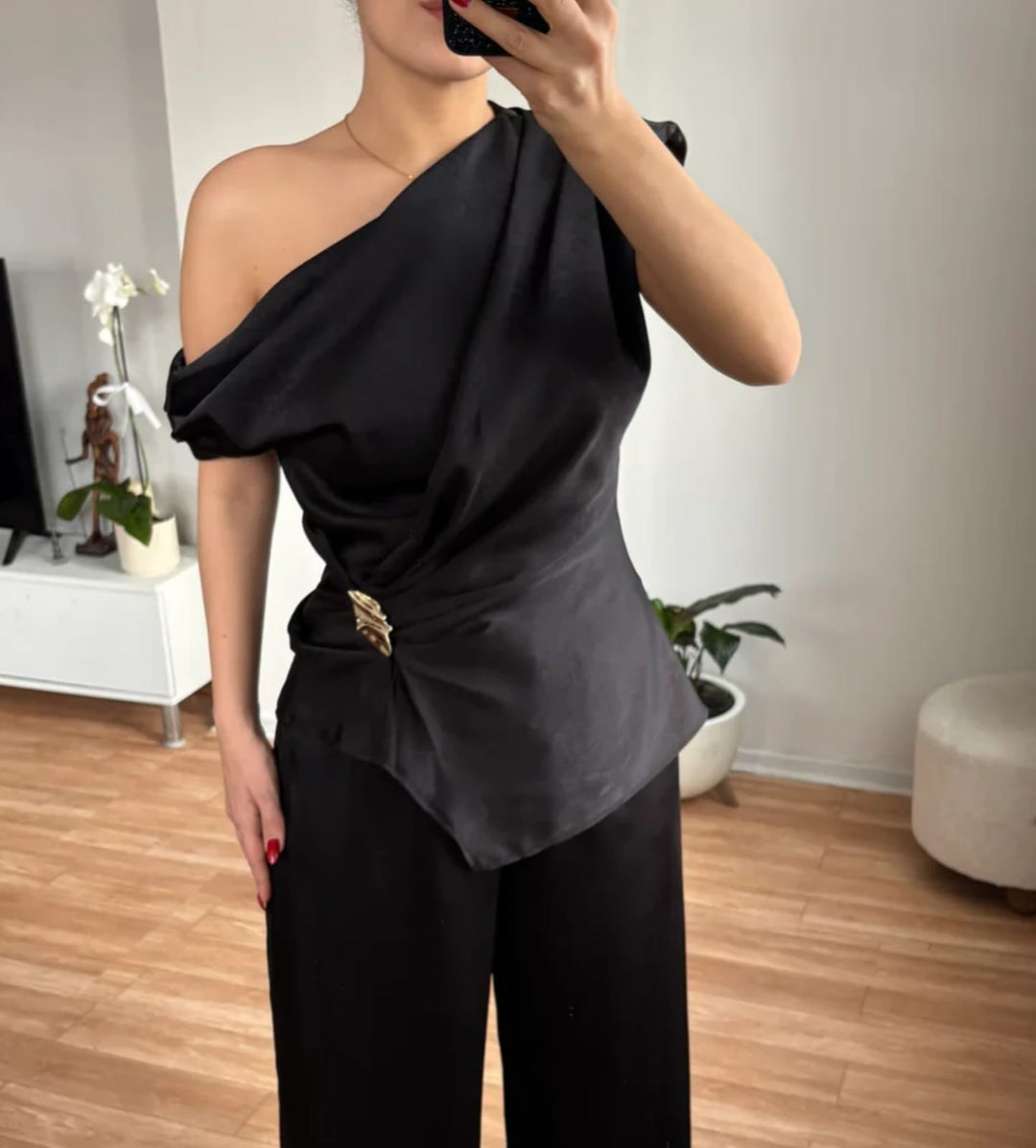 Woman wearing a folded gold brooch at the waist of a black one-shoulder top 