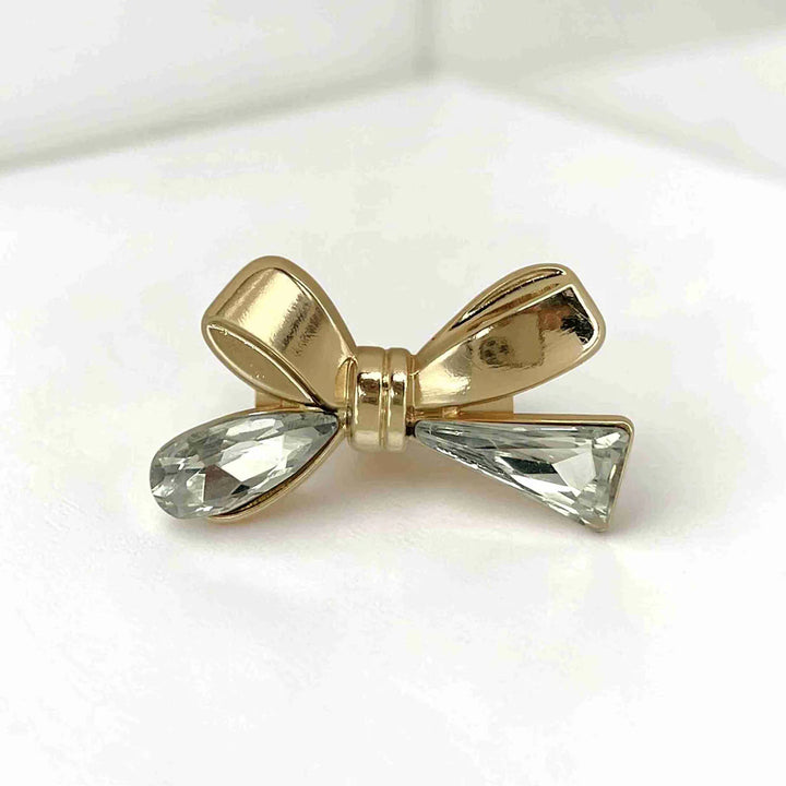 ANI Accessories gold bow brooch for women with teardrop and triangle crystal tails, on grey with white color background 