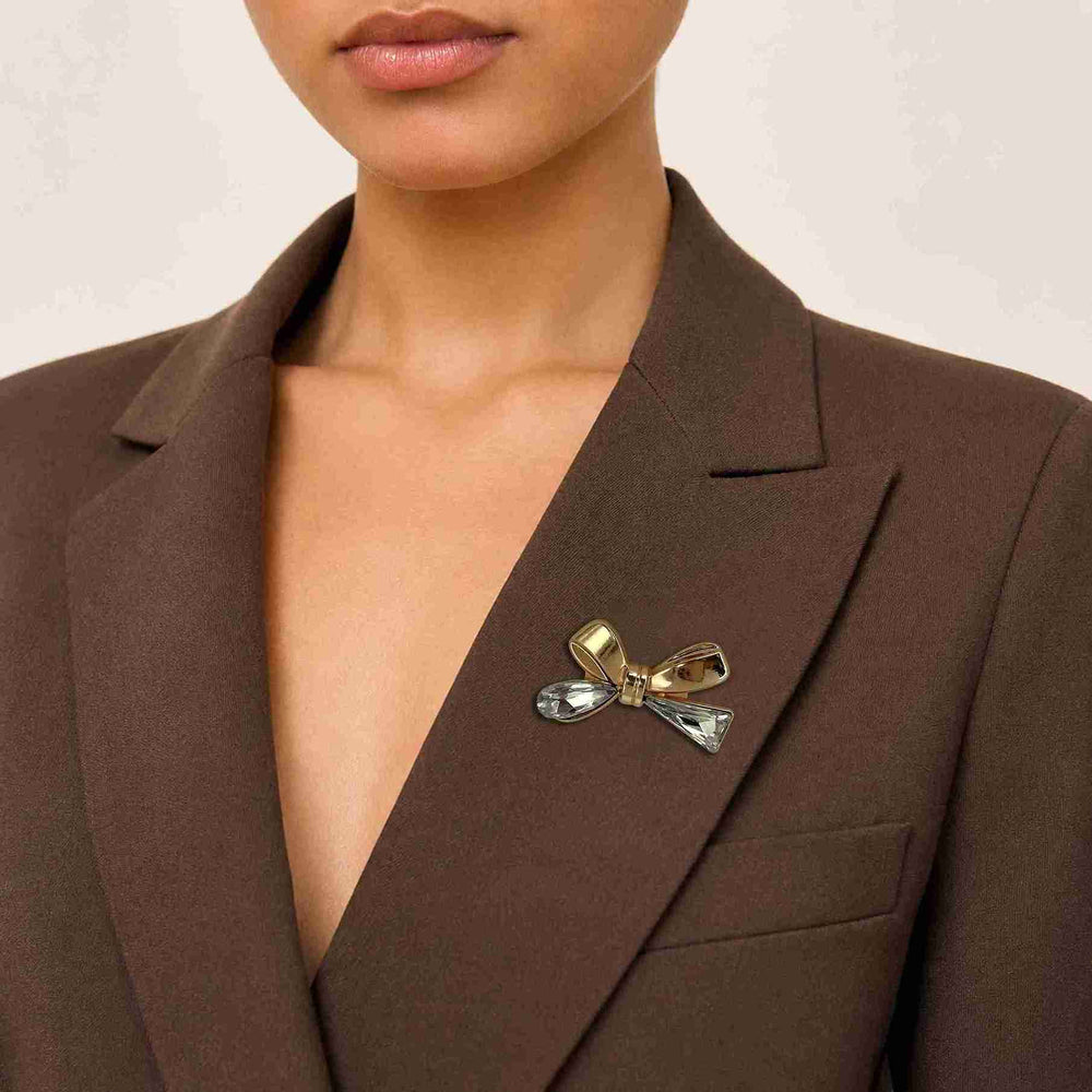 ANI Accessories gold bow brooch pinned on the lapel of a woman's brown blazer 