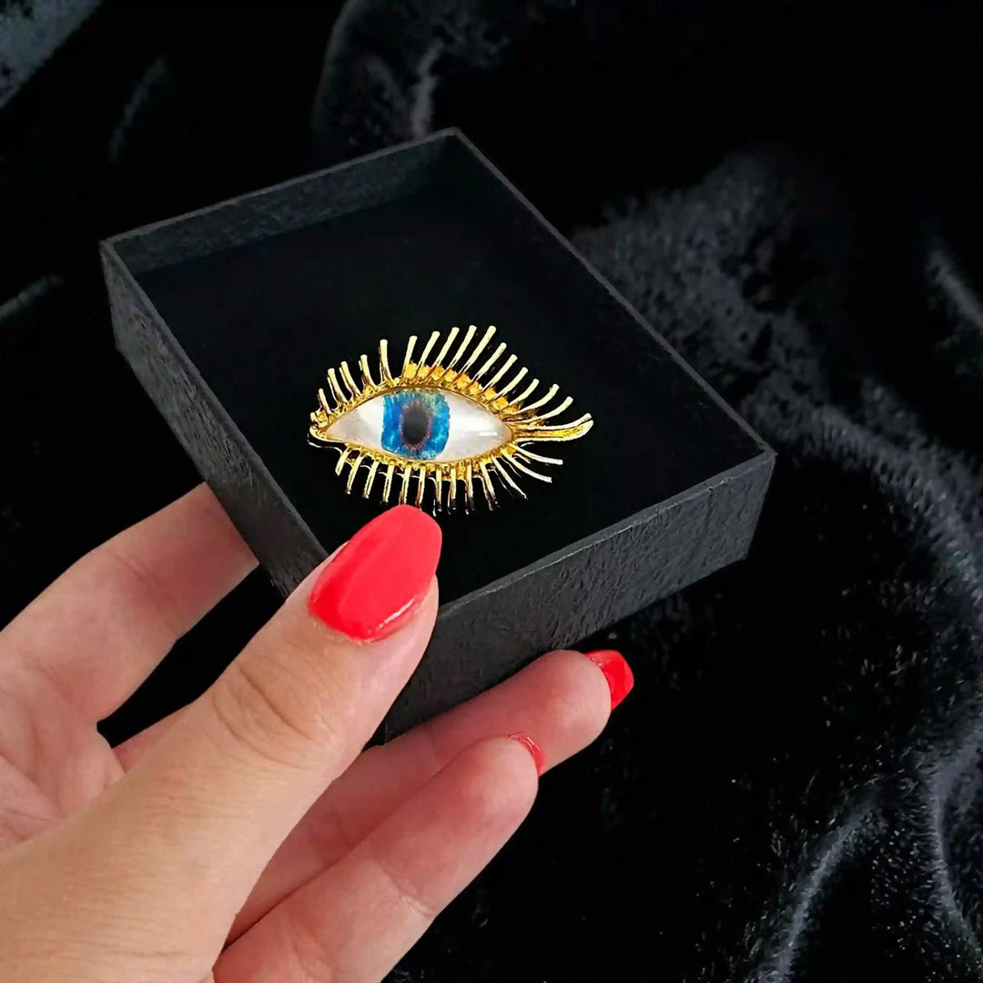 ANI Accessories gold evil eye brooch in a black box held in hand 