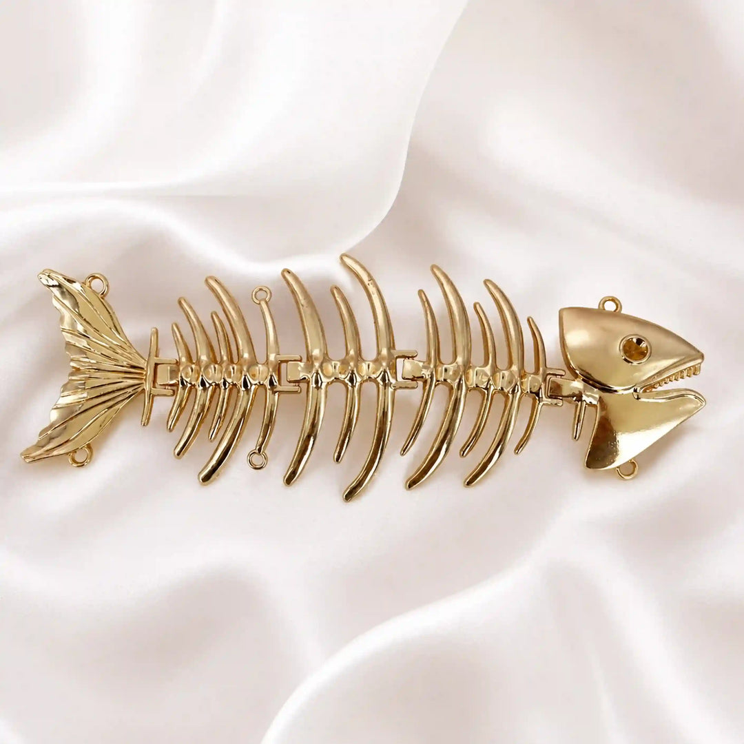 ANI Accessories fish skeleton sew brooch in high-shine gold on white satin 