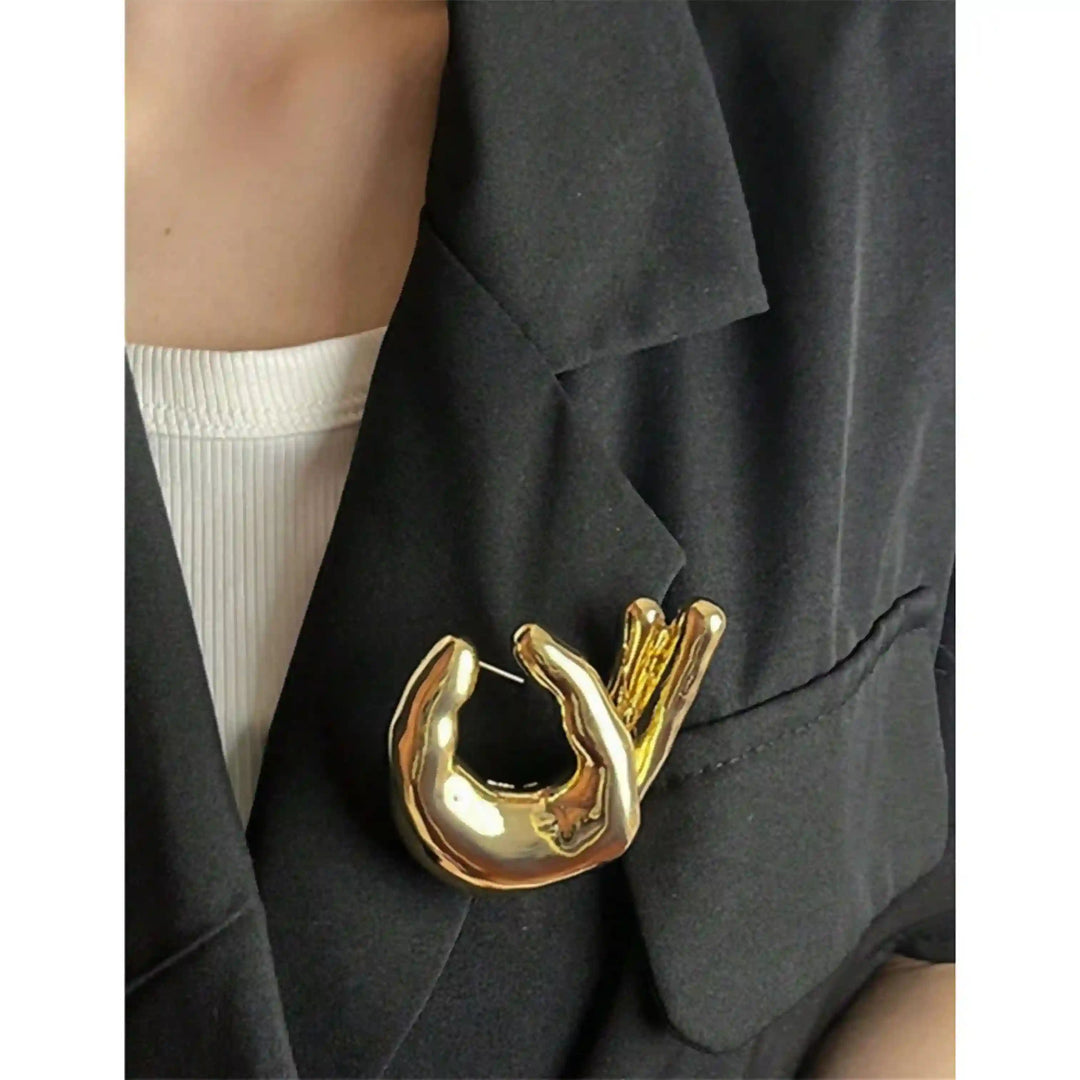 ANI Accessories gold hand gesture lapel pin worn on a black waistcoat over a white shirt 
