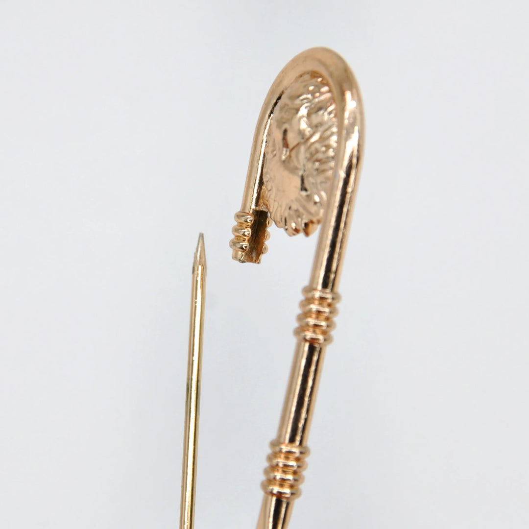 Close-up of the gold lion head medallion on a big safety pin with white color background 