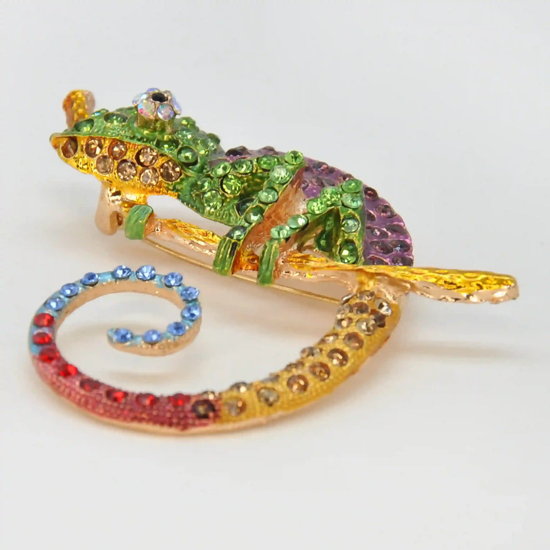 Side view of the green rhinestone chameleon brooch on a gold branch with white color background 