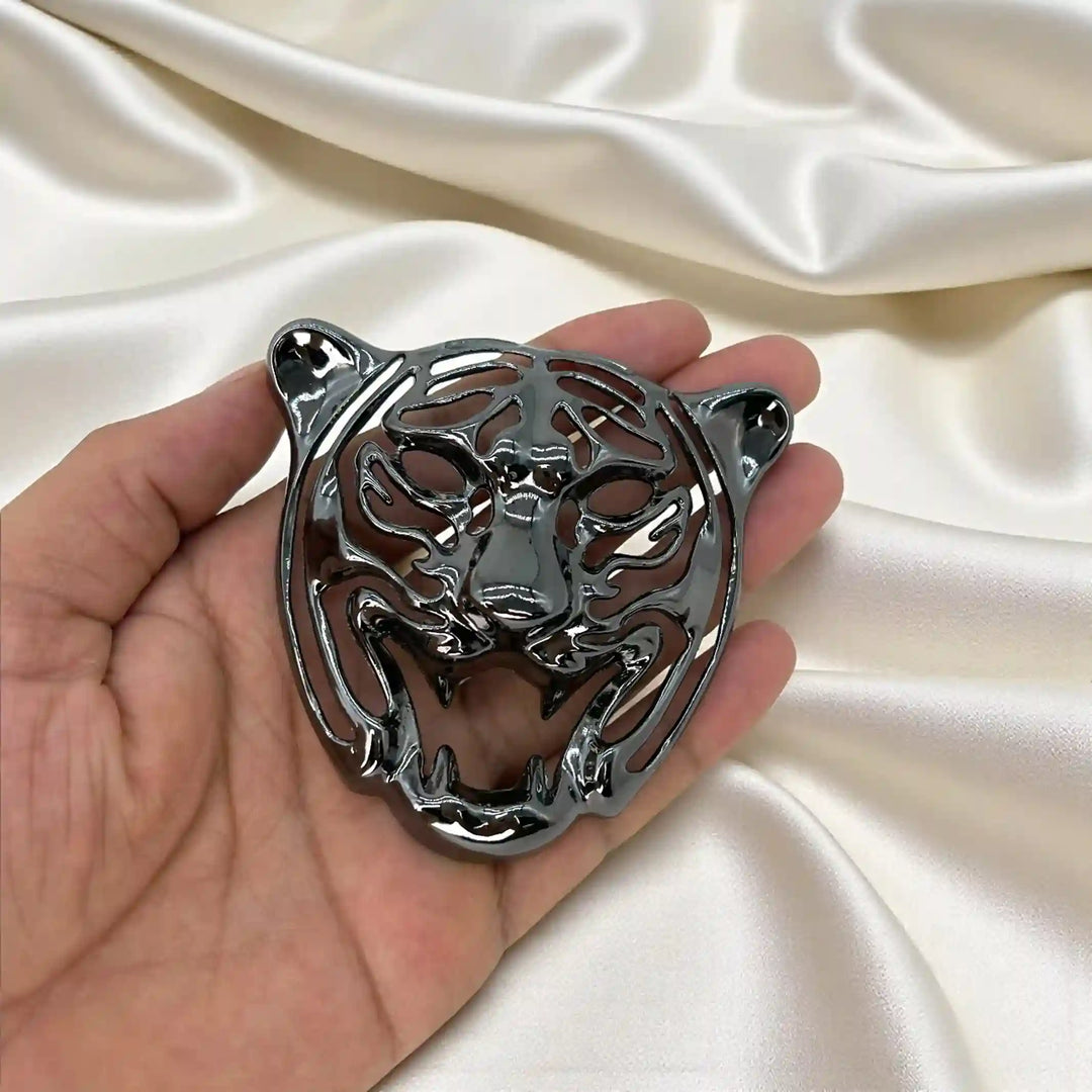 Gunmetal tiger head emblem with roaring face held in hand on white satin with white color background 