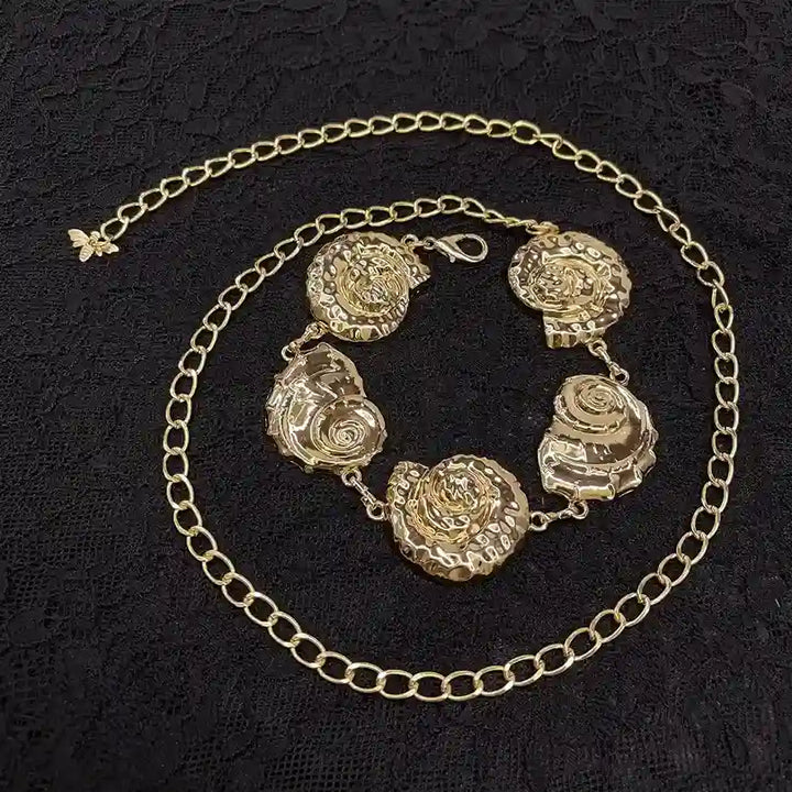ANI Accessories hammered gold belt with five spiral shells laid on black fabric
