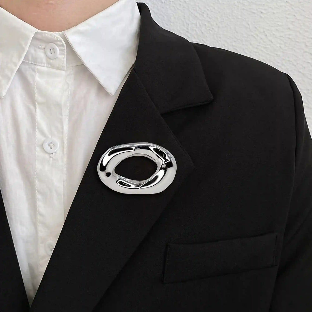ANI Accessories minimalist silver brooch pinned on a black blazer over a white shirt 
