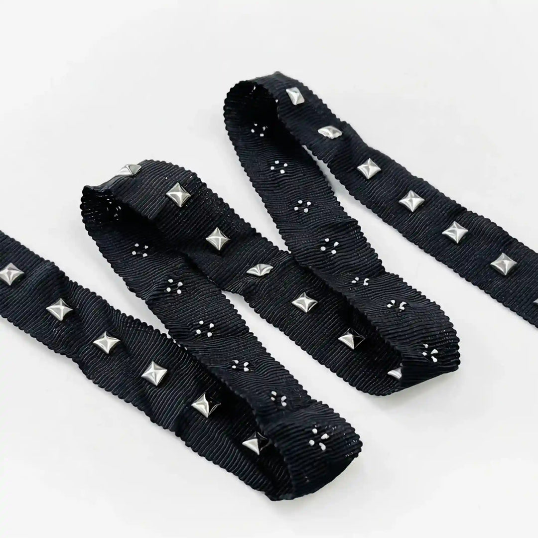 ANI Accessories pyramid studs for clothing on black ribbon, folded in a zigzag with white color background 