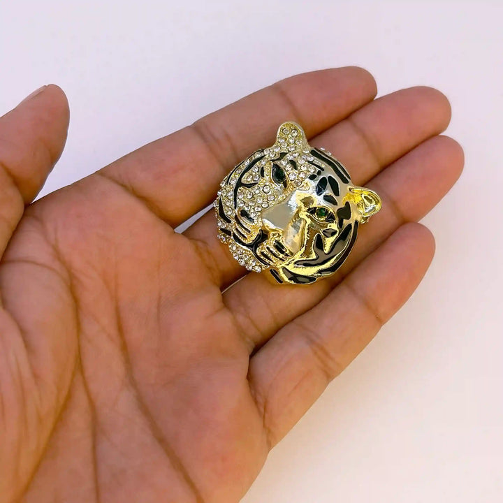 Shiny gold tiger head brooch held in hand to show its small size with white color background 