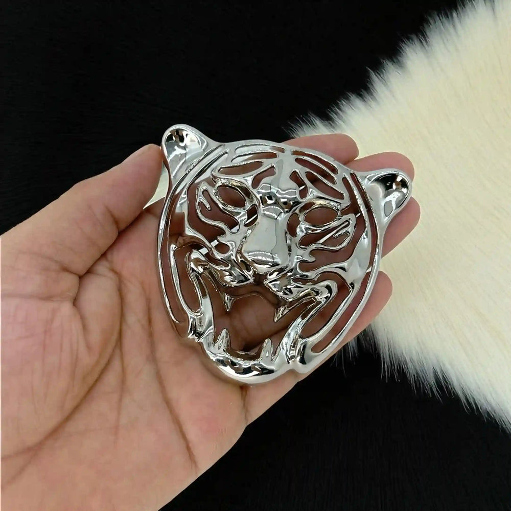 Silver tiger face emblem with laser-cut stripes held in hand over white fur with white color background 