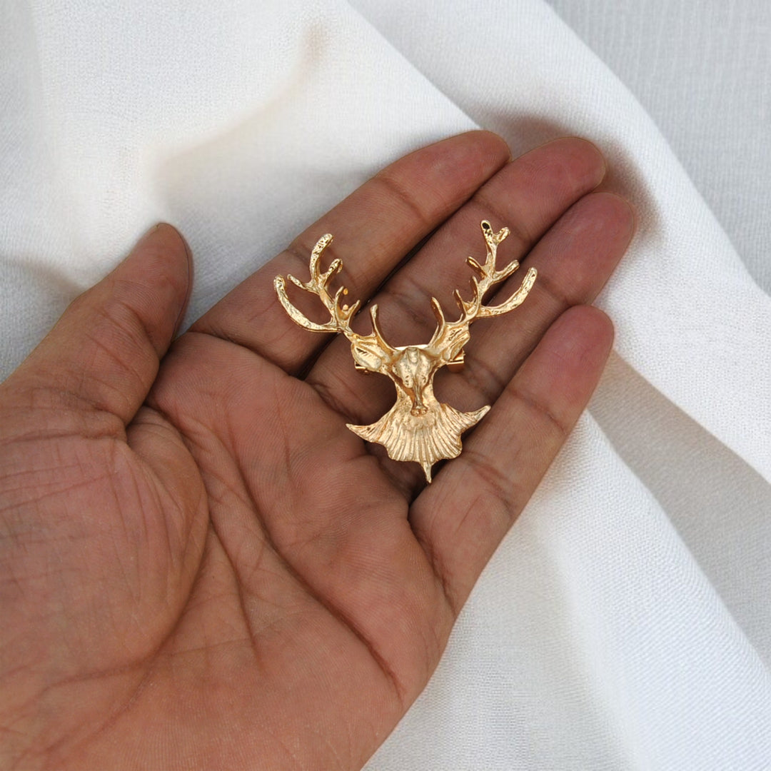 Gold stag brooch held in hand to show its size with white color background 