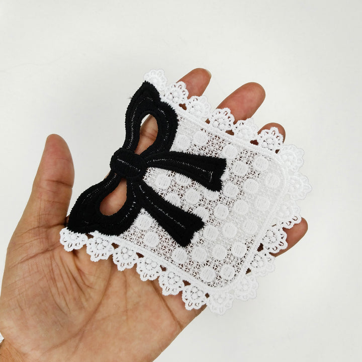 ANI Accessories white pocket patch with black bow held in an open palm to show its size  with white color background 