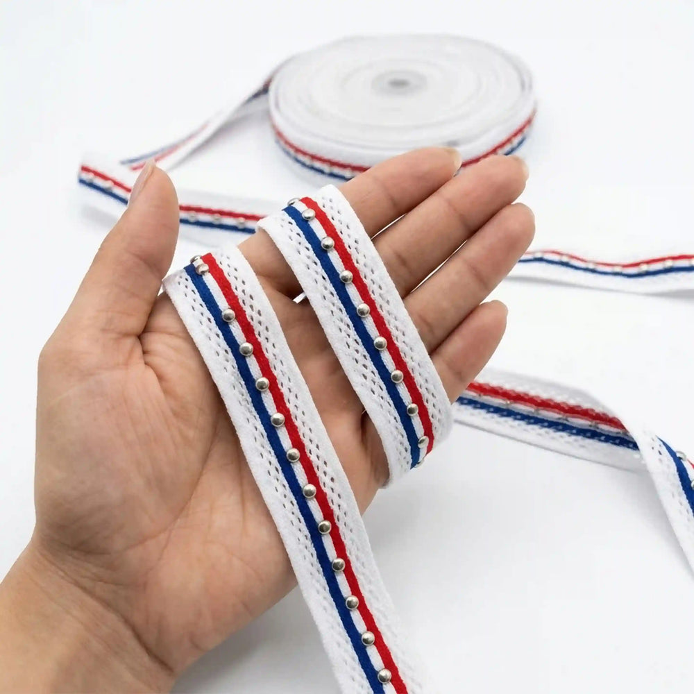 ANI Accessories white lace border with red and blue stripes held in hand next to the roll with white color background 